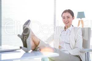 Cheerful businesswoman with legs on desk looking at camera