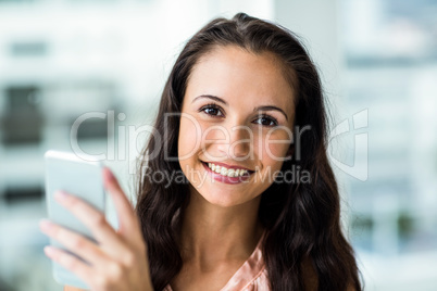 Smiling woman using smartphone and looking at camera