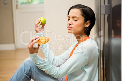 Unsettled brunette holding apple and dessert