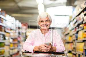 Senior woman using phone while pushing cart