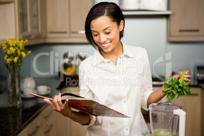 Smiling brunette reading book and preparing smoothie