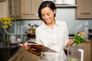 Smiling brunette reading book and preparing smoothie