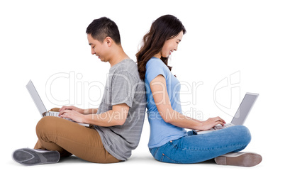 Happy young couple using laptop while sitting back to back