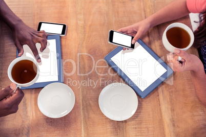 Colleagues holding coffee cups while using technologies at desk