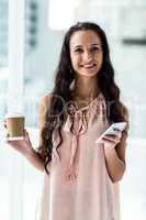 Smart woman using smartphone holding disposable cup