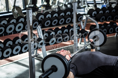 Muscular man lifting barebell while lying on bench