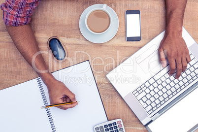 Businessman writing on book while working on laptop