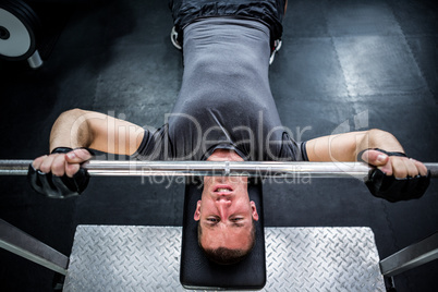 Muscular man lifting barebell while lying on bench