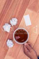 Cropped hand holding coffee cup by paper balls on desk