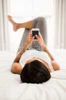 Brunette lying on bed and using smartphone