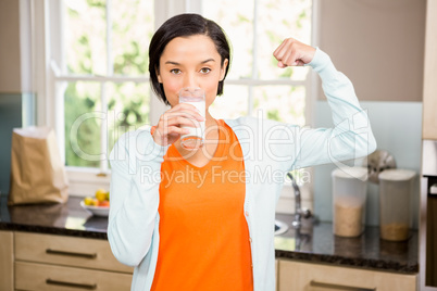 Happy brunette drinking milk and showing bicep