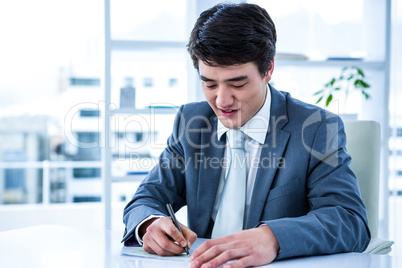 Smiling asian businessman completing a cheque