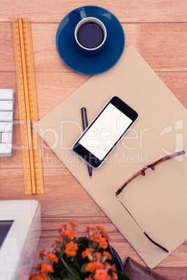 Smartphone by eye glasses on paper by coffee cup at desk