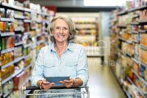 Smiling senior woman with cart using tablet