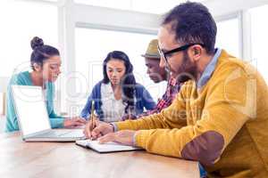 Business man writing in book while sitting with colleagues