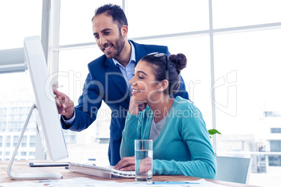 Happy businessman pointing and explaining to coworker over PC