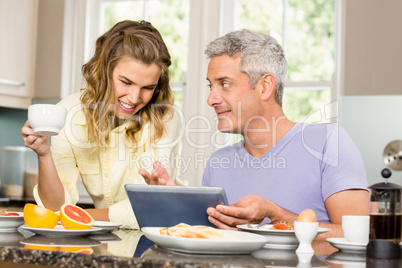 Happy couple using tablet and having breakfast