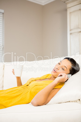 Smiling brunette on a phone call holding cup