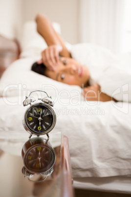 Alarm clock against brunette on bed