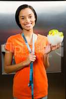Smiling brunette with tape measure around neck holding bowl of s