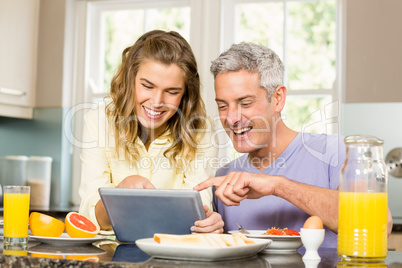 Happy couple using tablet and having breakfast