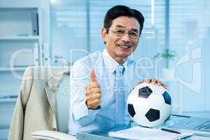 Asian businessman holding soccer ball with thumps up