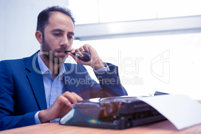 Businessman using typewriter while holding smoking pipe