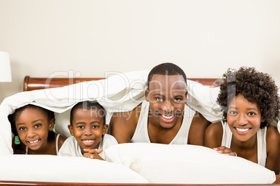 Cute family resting on bed under blanket