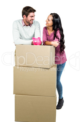Smiling couple holding on boxes with piggy saver