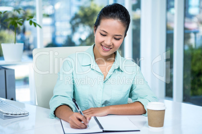 Smiling businesswoman writing notes with a coffee