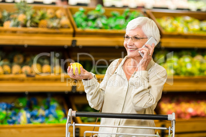 Old woman having a phone call while holding an apple