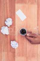 Cropped hand of businessman holding coffee cup by paper balls