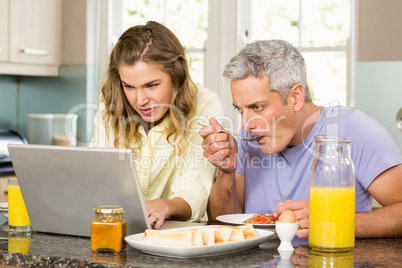 Happy couple using laptop and having breakfast