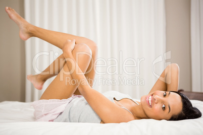 Smiling brunette on bed touching legs