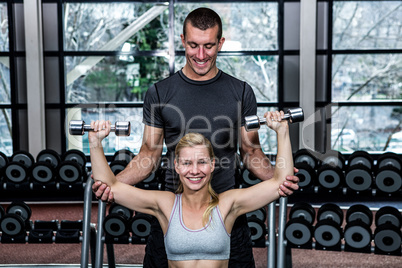 Fit woman doing dumbbells exercise with trainer