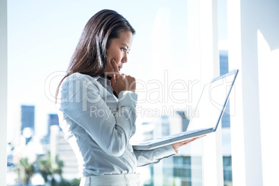 Businesswoman with finger on cheek using laptop