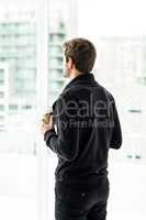 Man holding disposable cup looking out window