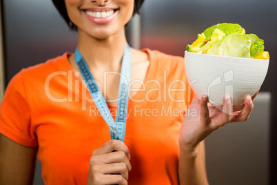 Smiling brunette with tape measure around neck holding bowl of s