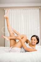 Smiling brunette on bed touching legs