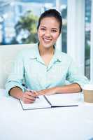 Smiling businesswoman writing notes with a coffee