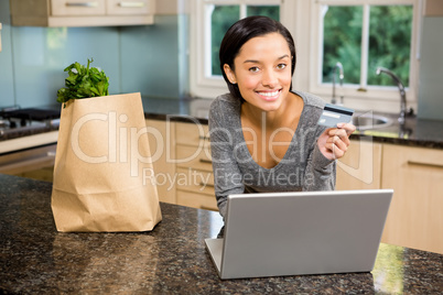 Smiling brunette using laptop and holding credit card