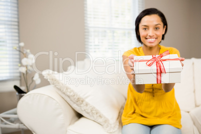 Smiling brunette holding gift to the camera