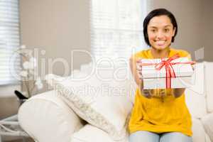 Smiling brunette holding gift to the camera