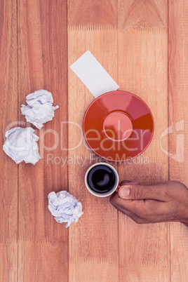 Hand holding coffee cup by crumbled paper and saucer on desk