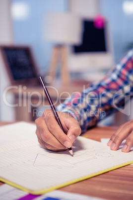 Cropped hand of businessman drawing house in book