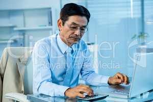Focused asian businessman using calculator and laptop