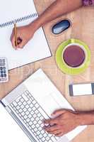 Businessman working on laptop while writing on book