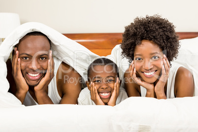 Happy family posing in bed under blanket