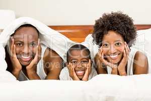 Happy family posing in bed under blanket