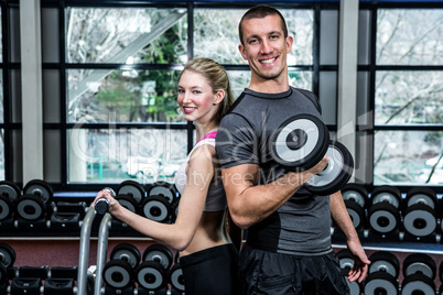 Fit couple lifting dumbbells back to back